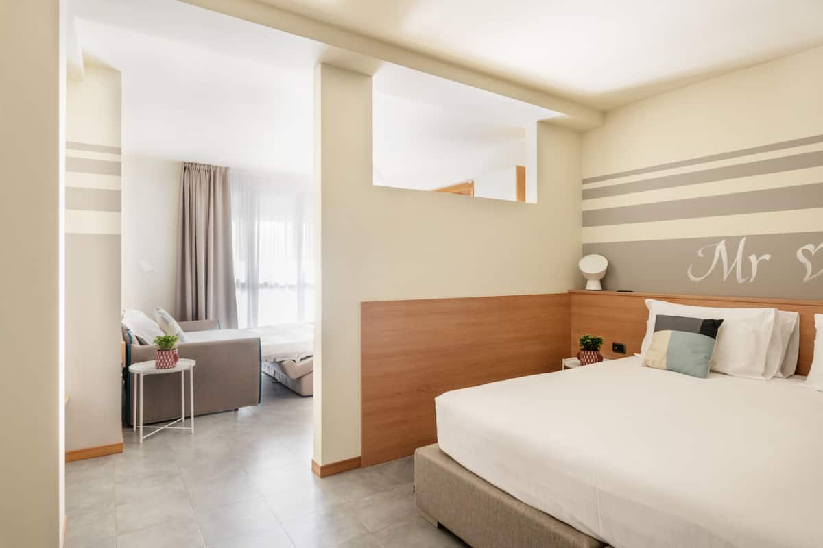 Habitación de hotel con una cama grande, una mesita con una planta, un sofá y un espejo en la pared.