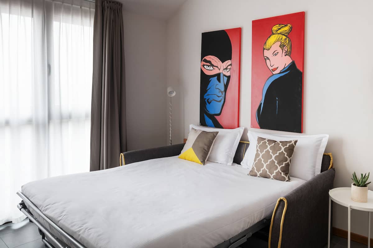 Un hotel moderno con una cama grande, una mesita de noche con una planta y dos cuadros coloridos en la pared.