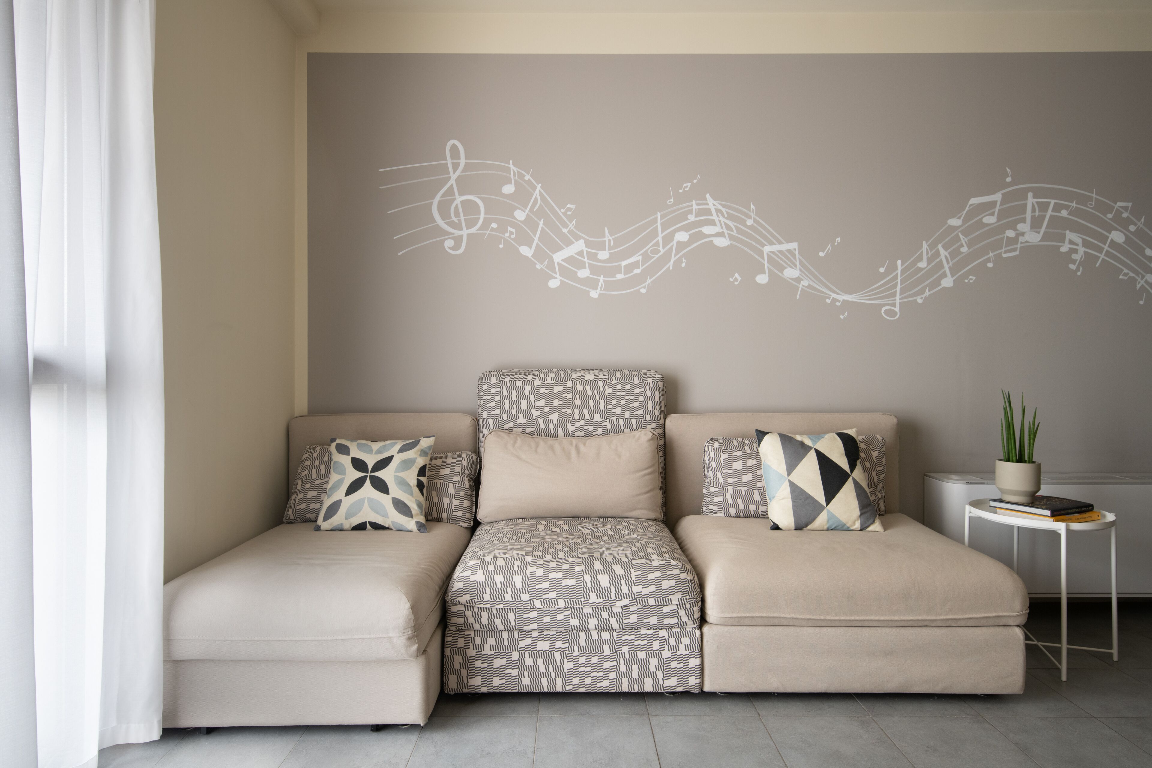 A modern living room with a sofa, patterned cushions, a wall mural, and a small side table with a plant.