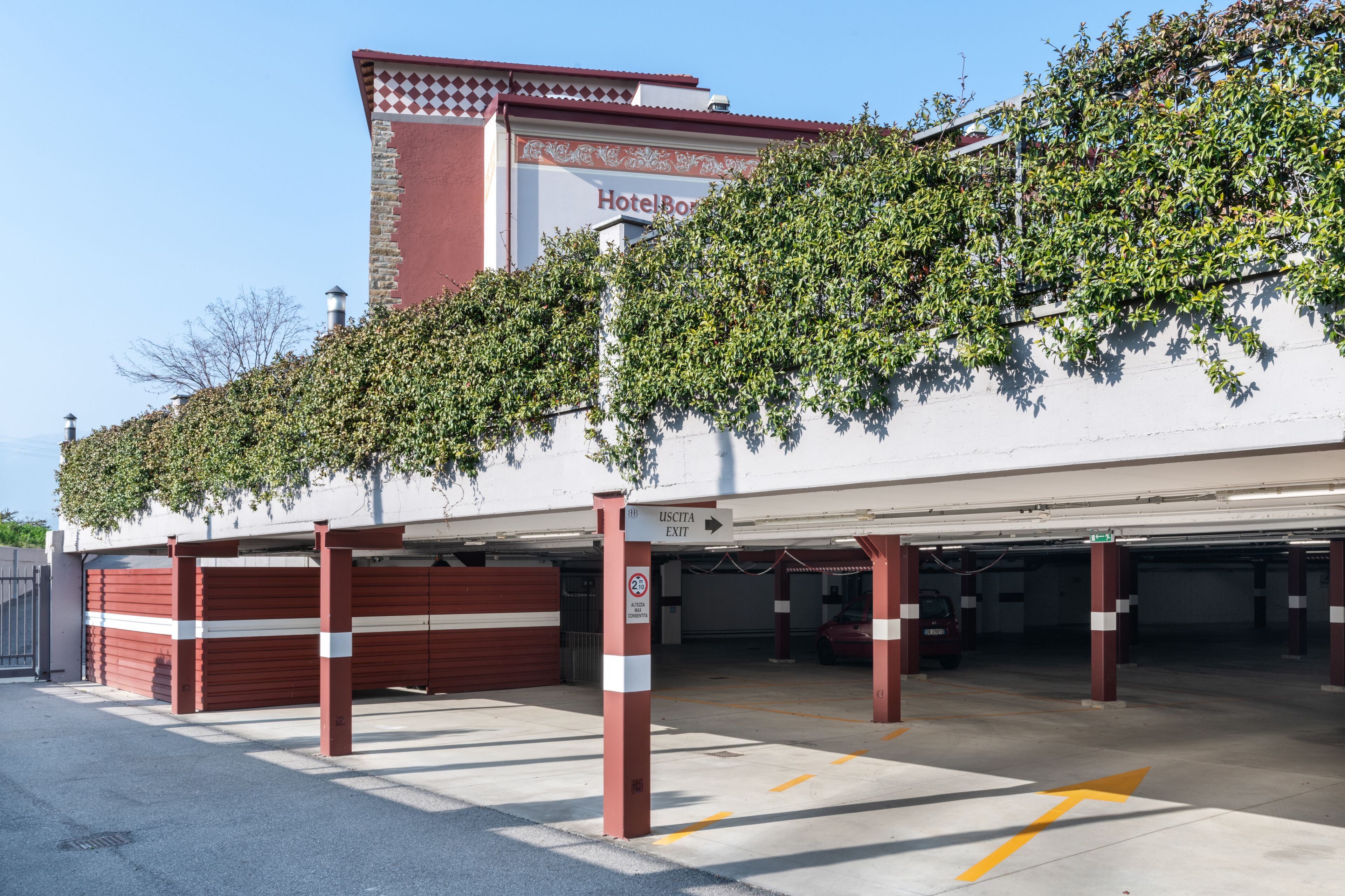 Un hôtel à la façade rouge et blanche, doté d’un parking couvert et d’un panneau indiquant la sortie.