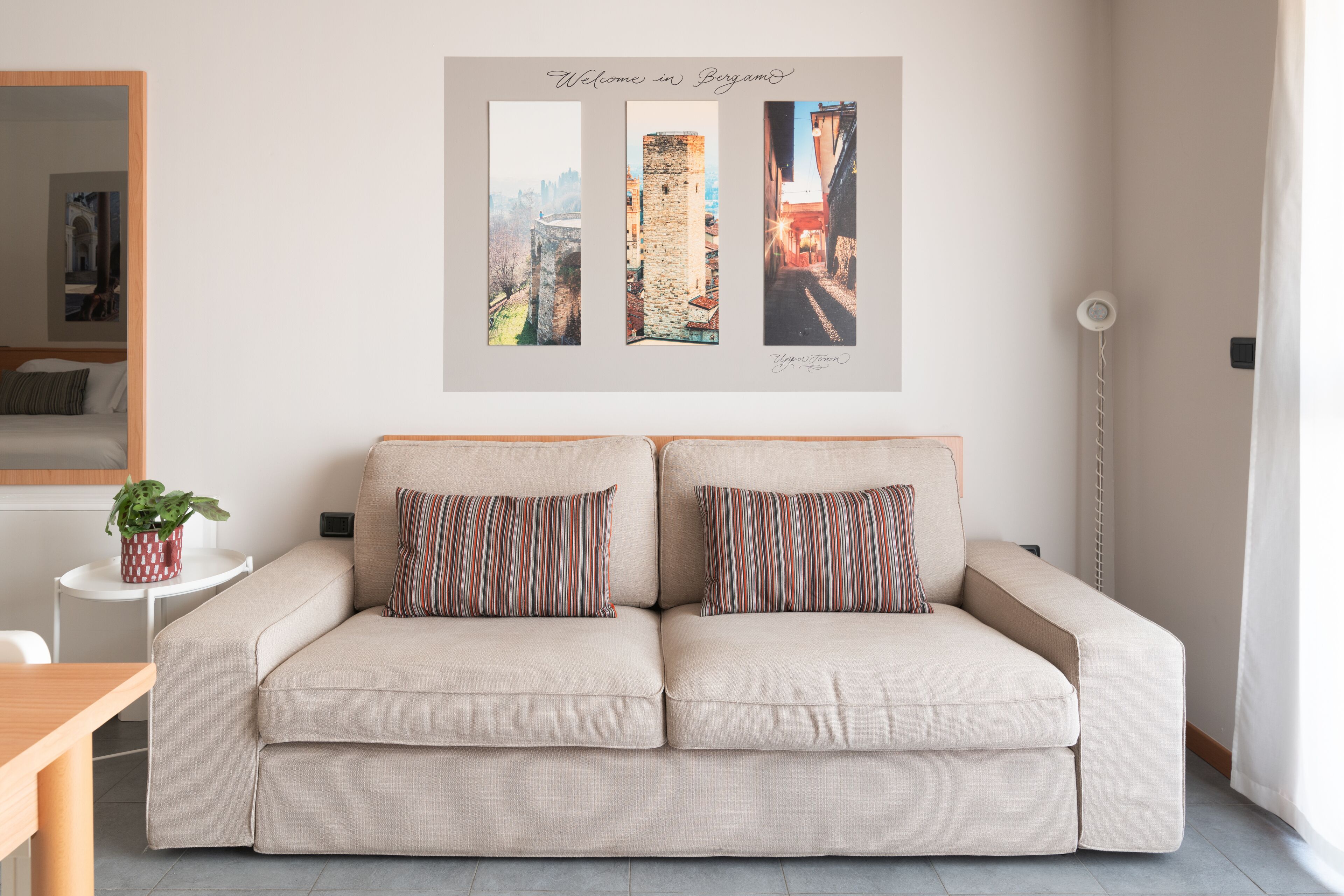 A beige sofa with striped pillows, a small side table with a plant, and a wall with three framed pictures.