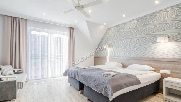 A modern bedroom with a bed, bedside tables, a ceiling fan, and a large window with curtains. - Helios Apartamenty (Ustka)