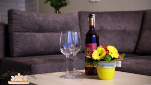 A bottle of wine, a glass, and a yellow flower arrangement on a table in a living room with a couch. - Helios Apartamenty (Ustka)
