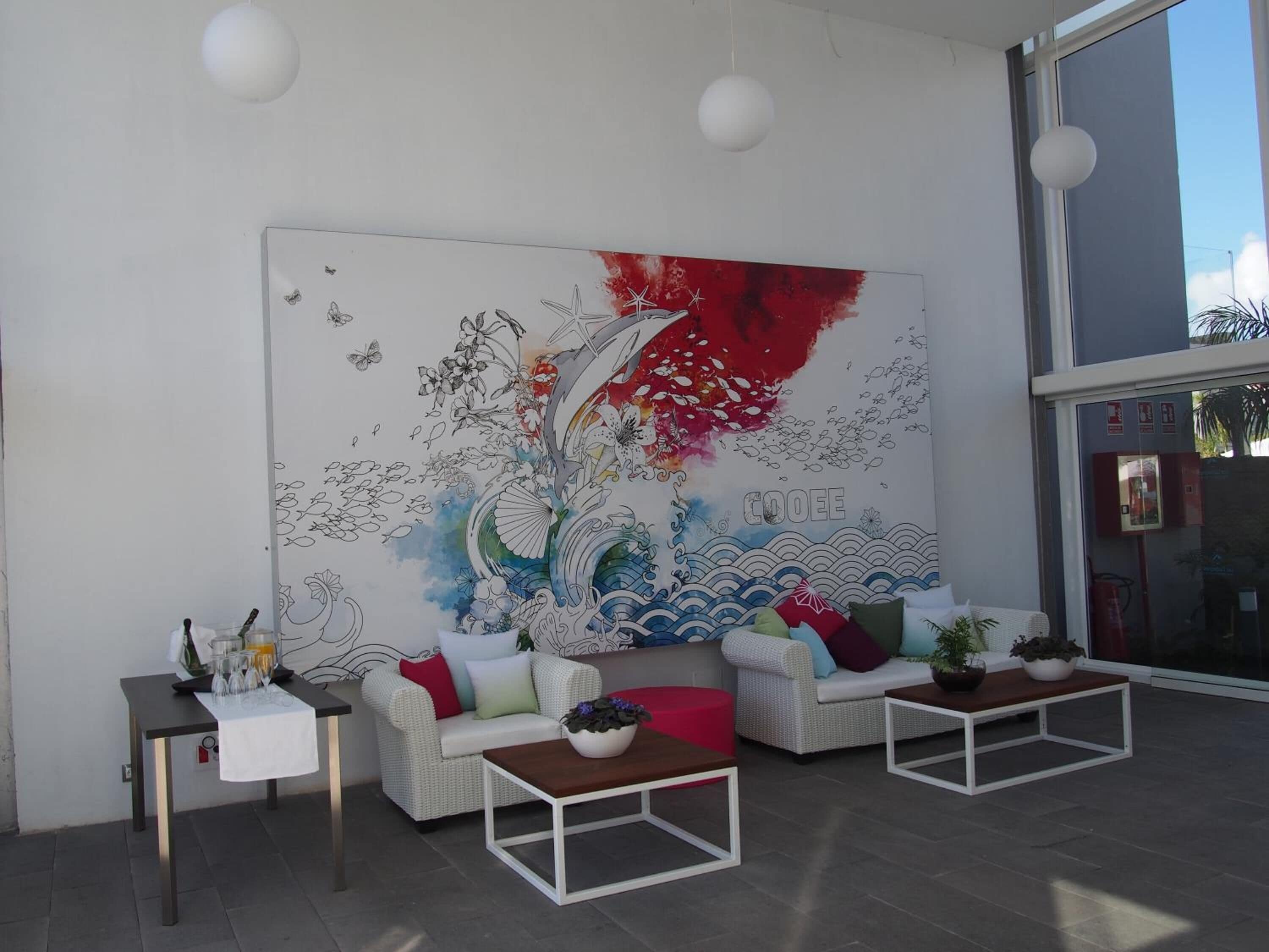 A modern lounge area with a large abstract painting, two sofas, a coffee table, and a small table with glasses and a bottle.