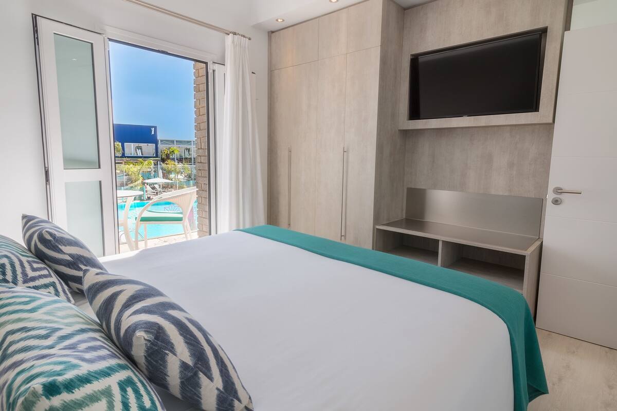 Une chambre d’hôtel avec un lit, une télévision, un balcon donnant sur une piscine et une porte coulissante.