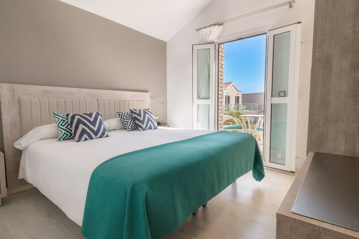 Une chambre à coucher avec un lit, une couvre-lit verte et une vue sur l’extérieur grâce à une porte-fenêtre coulissante.