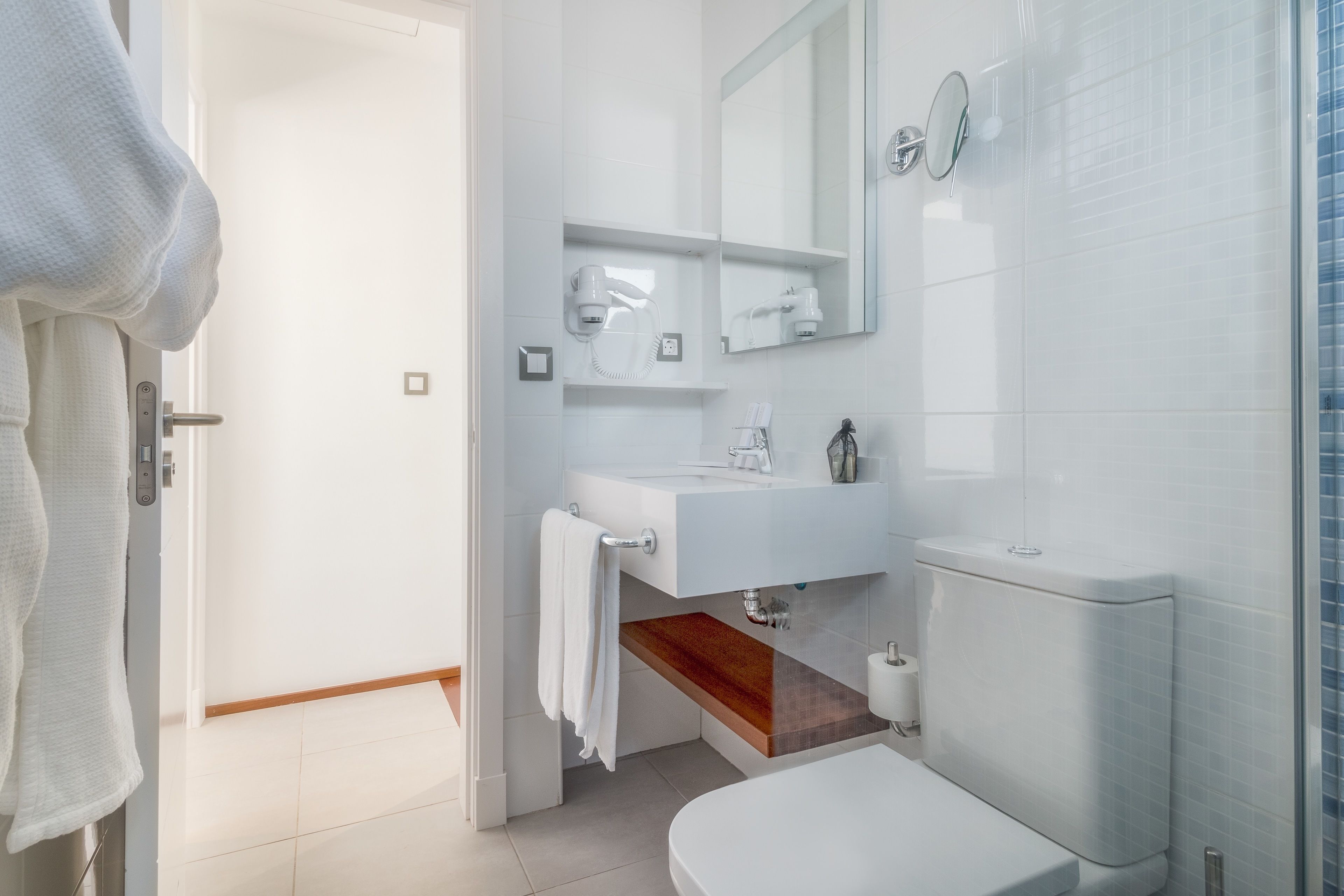 A modern bathroom with a white sink, a mirror, a towel rack, and a shower area.