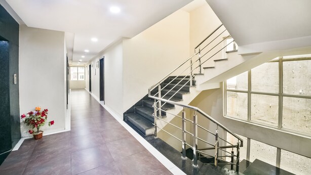 Un interior moderno de hotel con una escalera central, un largo pasillo y una planta en maceta.
