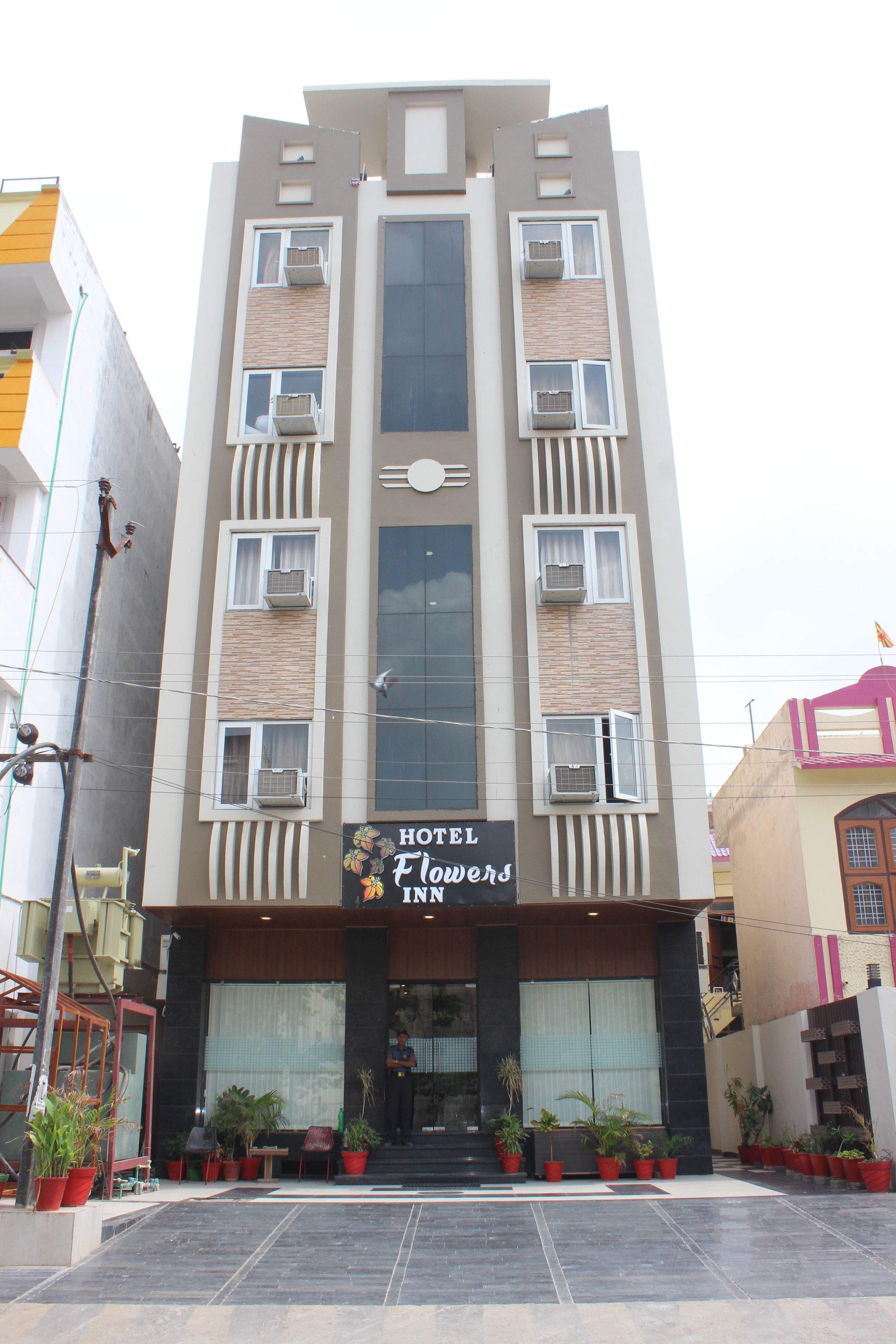 A hotel named Hotel Flowers Inn with a modern facade, multiple balconies, and potted plants at the entrance.