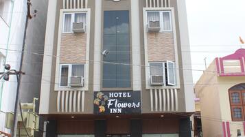 A hotel named Hotel Flowers Inn with a modern facade, multiple balconies, and potted plants at the entrance.