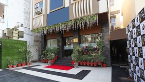 Entrada de hotel con alfombra roja, plantas en macetas y una escalera que lleva a la recepción.