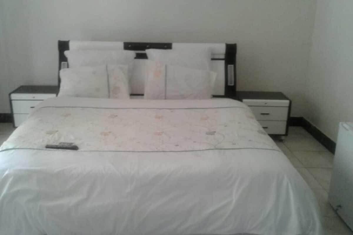 A standard hotel room with a bed, two bedside tables, a nightstand, and a small desk.
