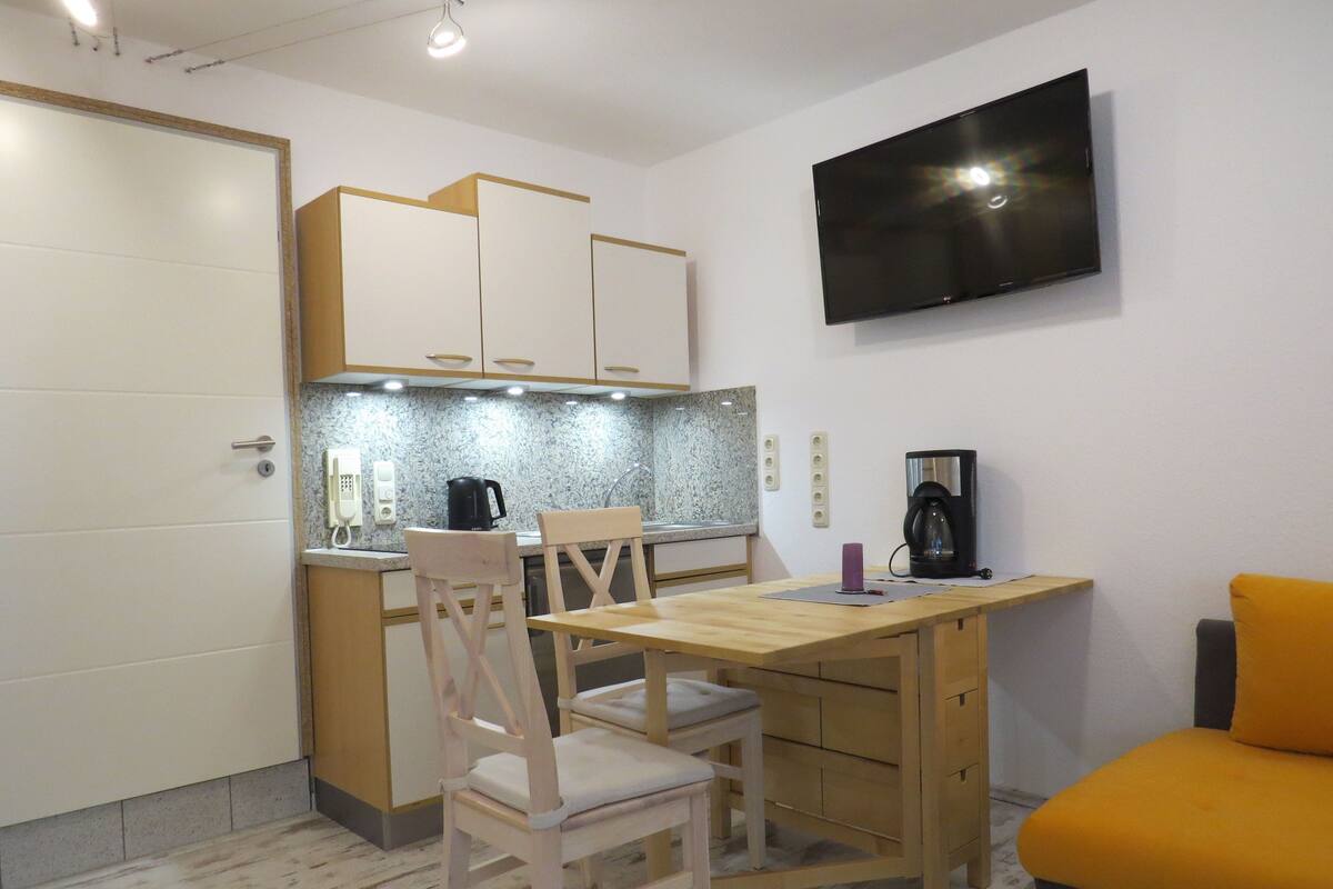 Una cocina compacta con zona de comedor, un televisor montado en la pared y un sofá en la esquina.