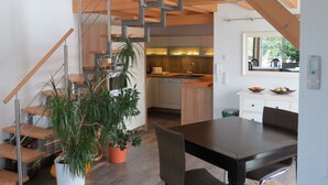 Una cocina moderna con vigas de madera, una escalera y un comedor con mesa y sillas.