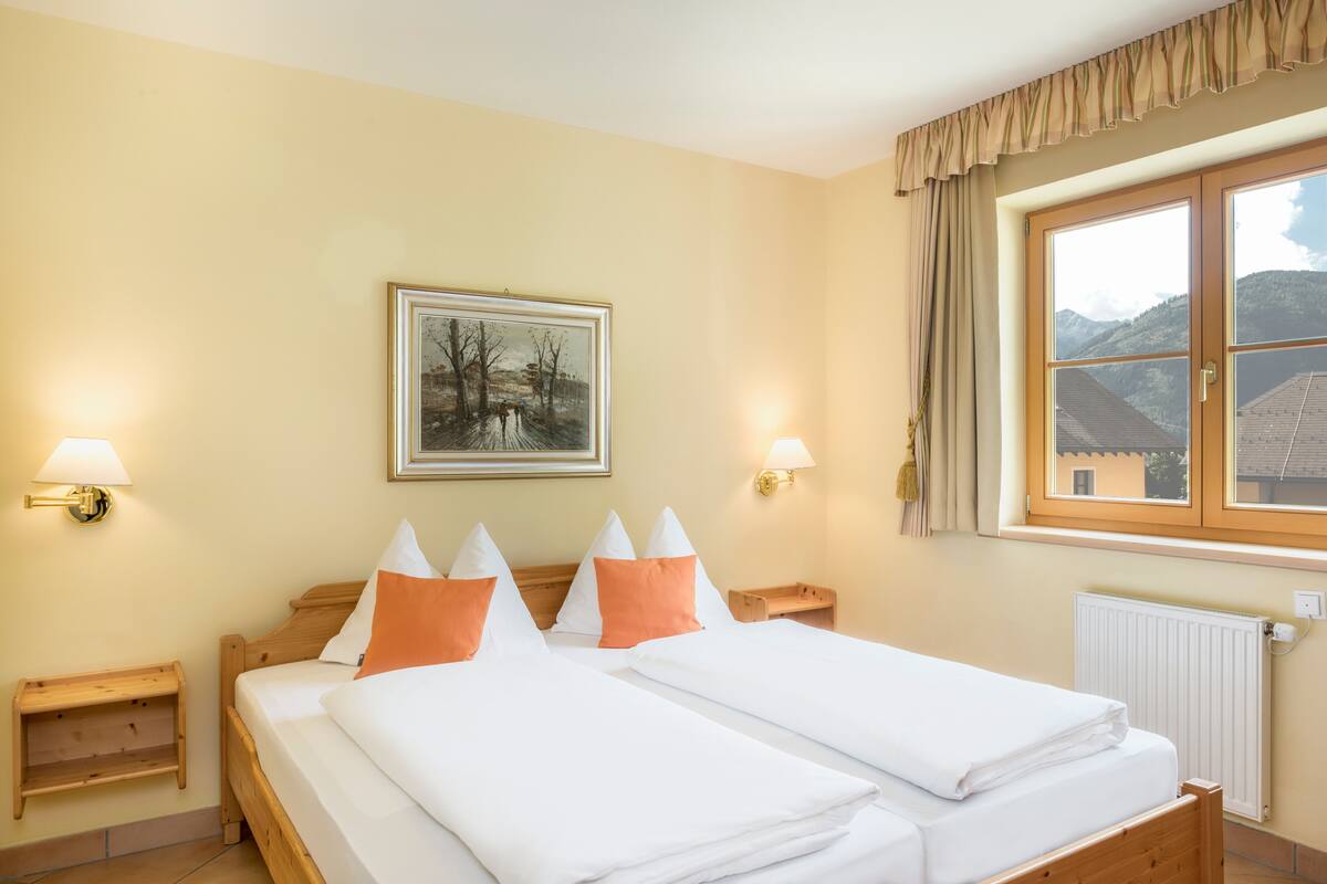 A hotel room with two beds, a painting on the wall, and a window with a mountain view.