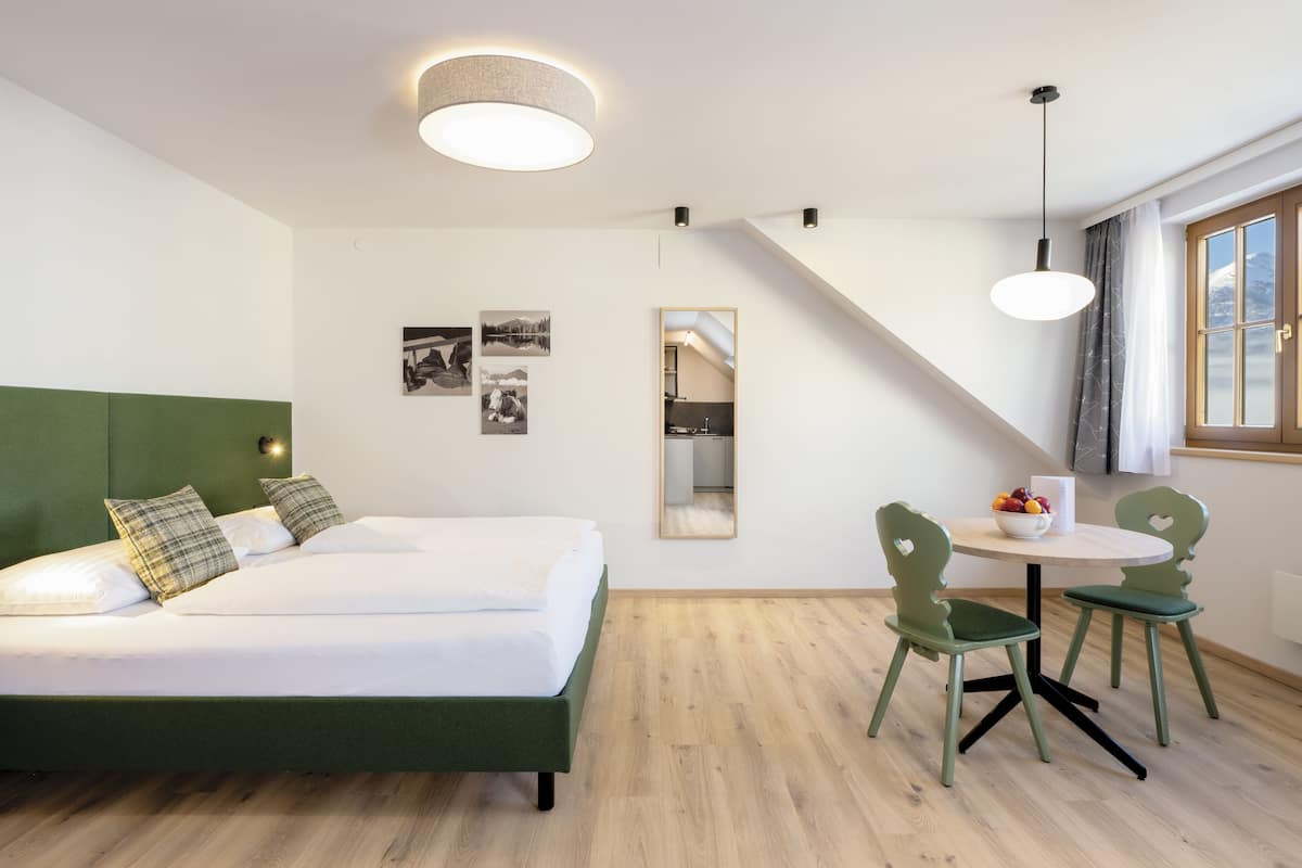 A modern hotel room with a bed, a dining table with chairs, a mirror, and a staircase.