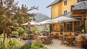 Une terrasse extérieure avec des tables et des chaises en bois, entourée de plantes et de fleurs en pot.