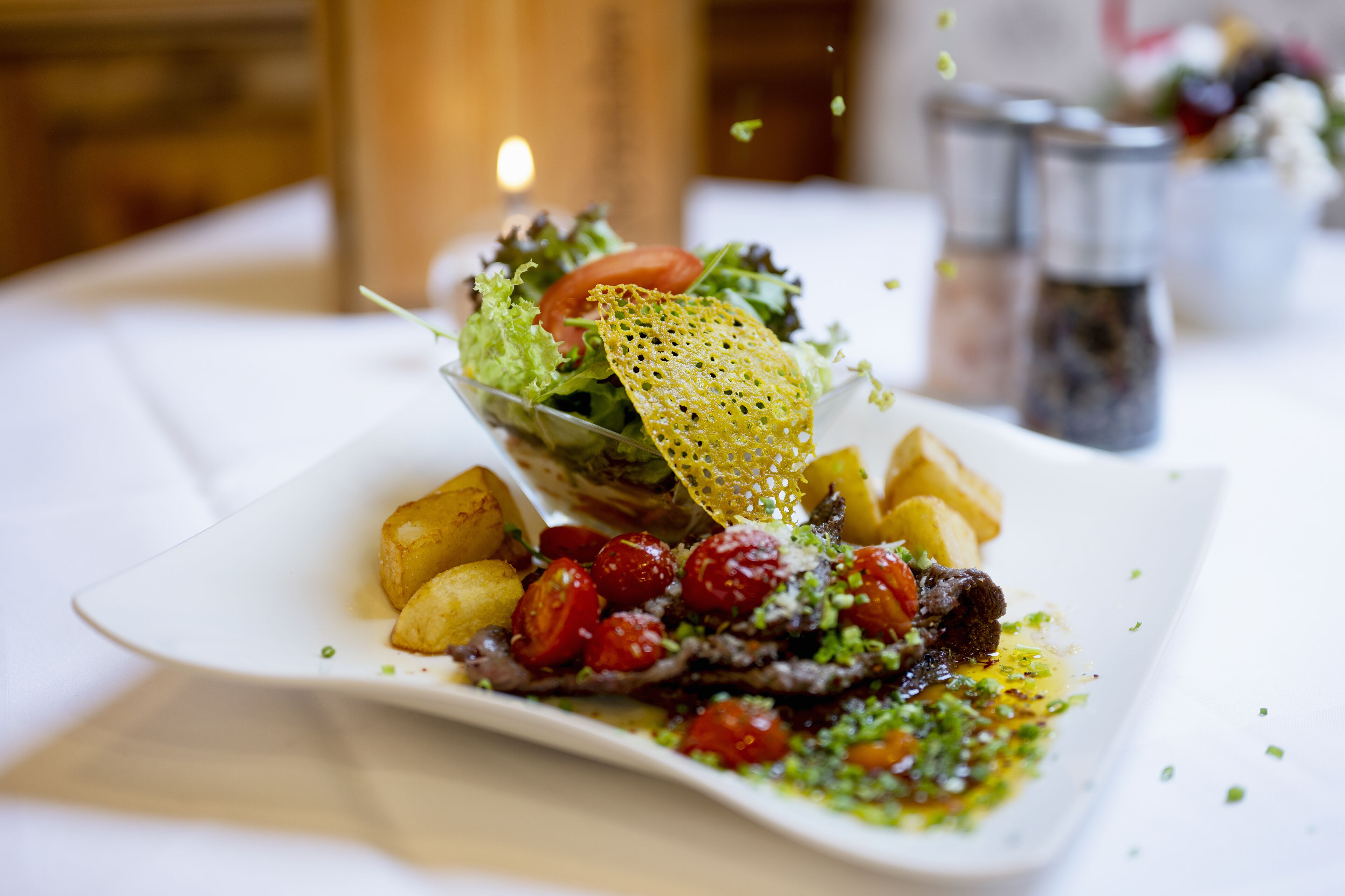 A plate of food with a salad, potatoes, and meat, garnished with herbs.