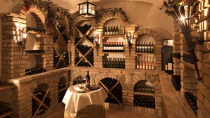 Une cave à vin avec des murs en briques, des étagères à bouteilles et une table où sont posées des bouteilles de vin.