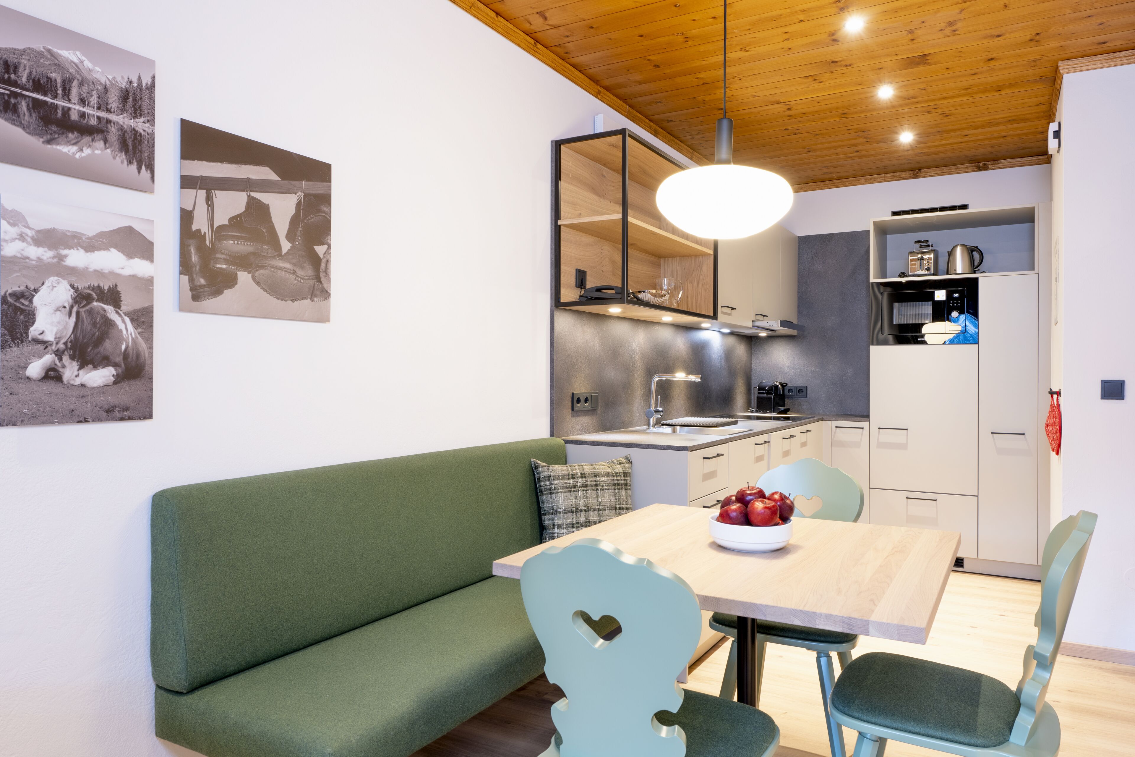 Une cuisine moderne avec un plafond en bois, un coin repas avec un canapé vert et une table sur laquelle sont posées des pommes.