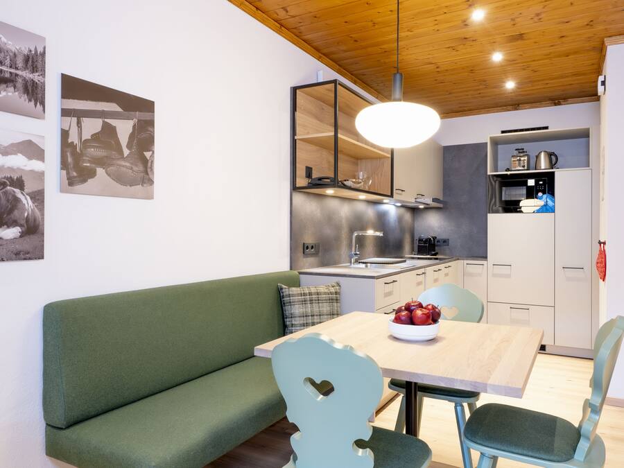 Une cuisine moderne avec un plafond en bois, un coin repas avec un canapé vert et une table sur laquelle sont posées des pommes.