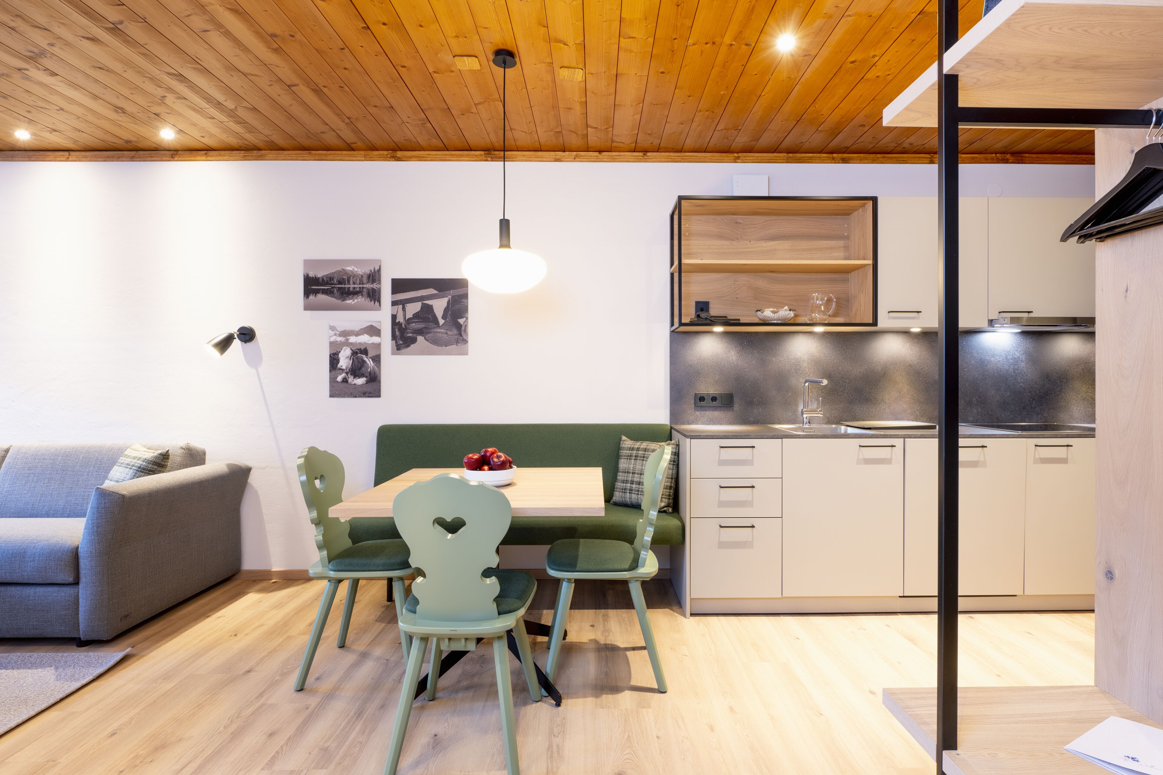 Un espacio habitable compacto con techo de madera, una kitchenette, un comedor con mesa y sillas, y un sofá.