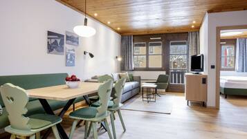 Una sala moderna con techo de madera, una zona de comedor con sillas verdes y una mesa de madera, un sofá y un televisor.