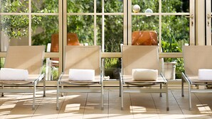 Un espace intérieur lumineux, aménagé avec des chaises et une table, et de grandes fenêtres offrant une vue sur la verdure environnante.