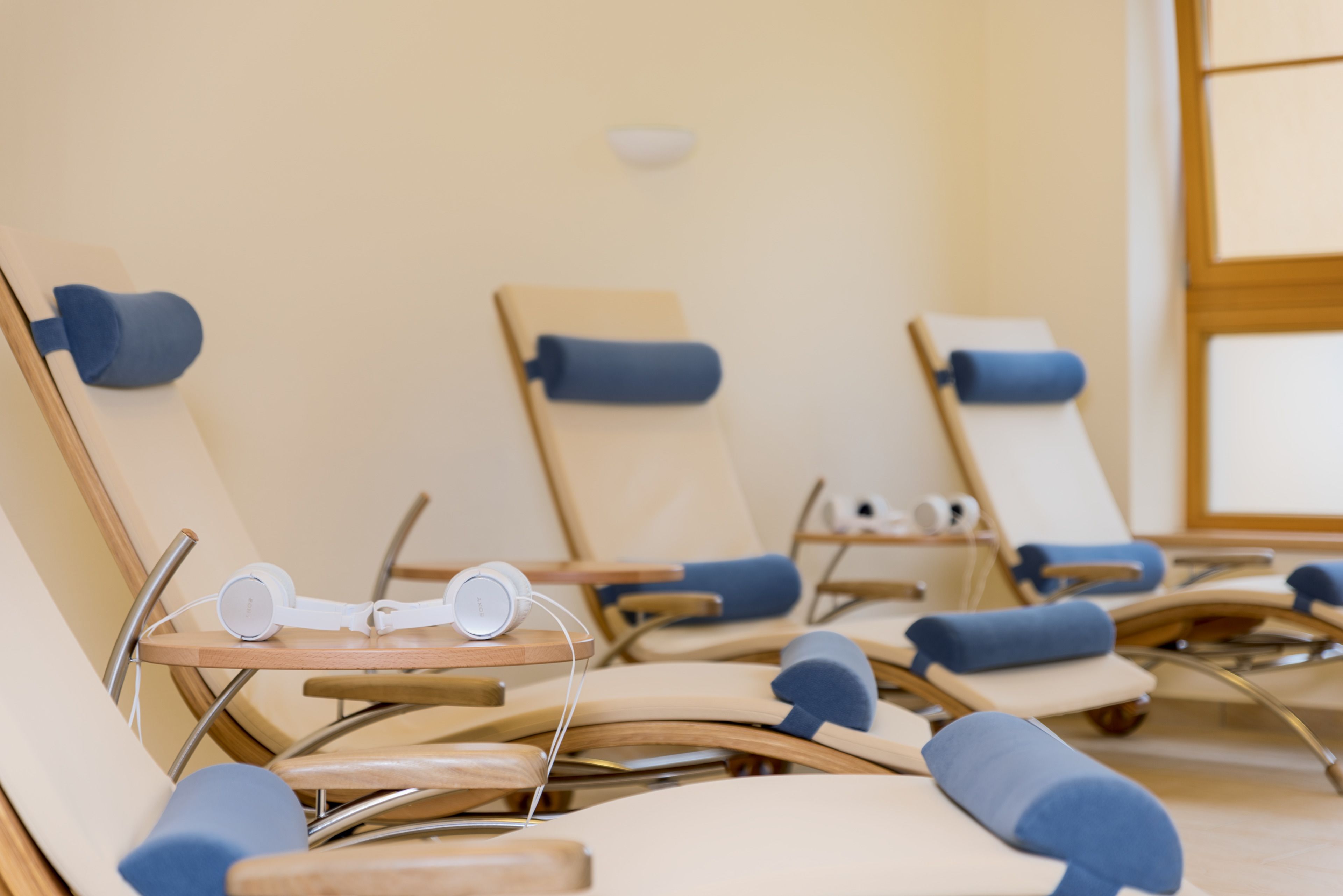 A row of sun loungers with blue cushions and a pair of white headphones on a table.