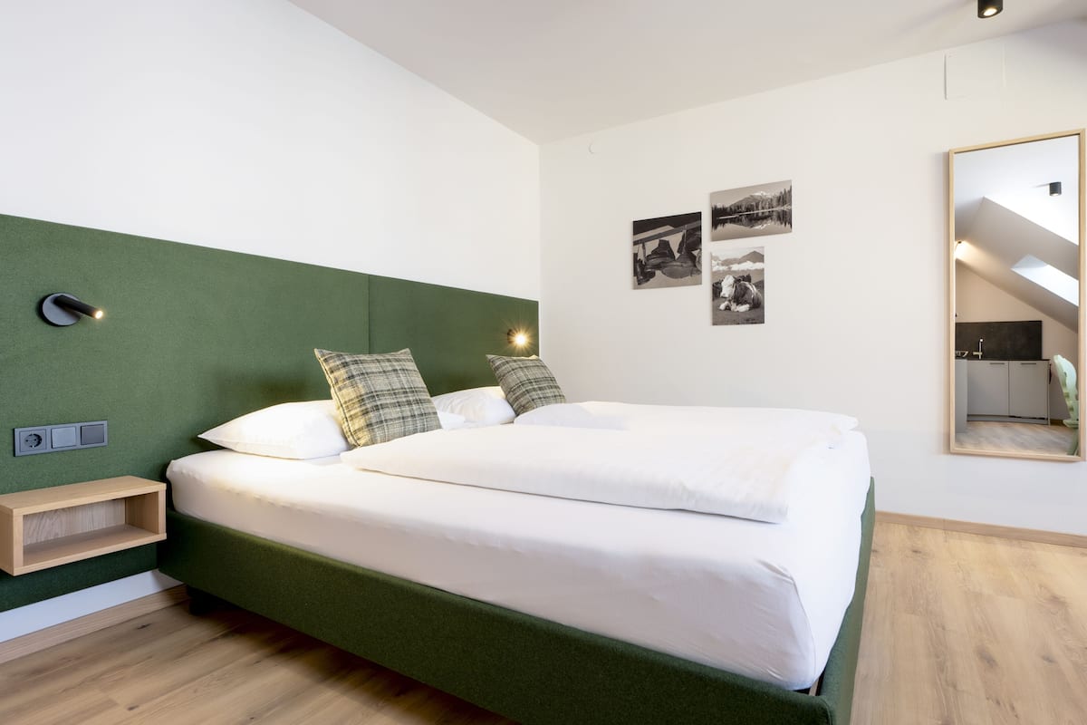 A modern hotel room with a large bed, a green headboard, a bedside table, and a mirror.