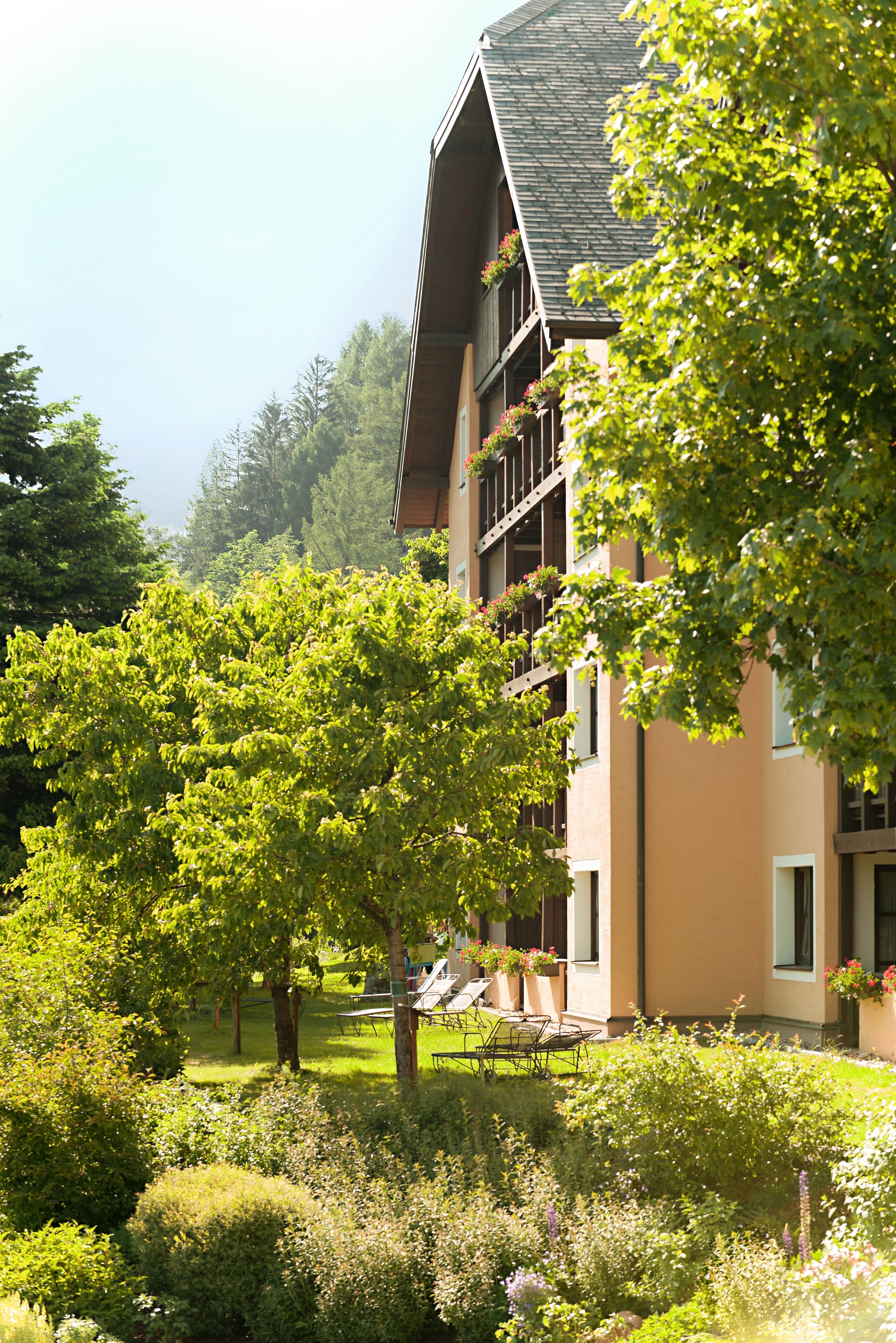 Un immeuble à plusieurs étages doté de balcons, entouré d’une végétation luxuriante et d’arbres.