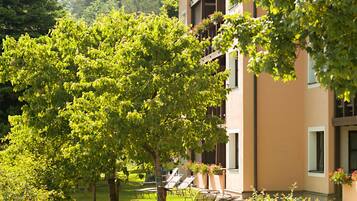 Un immeuble à plusieurs étages doté de balcons, entouré d’une végétation luxuriante et d’arbres.