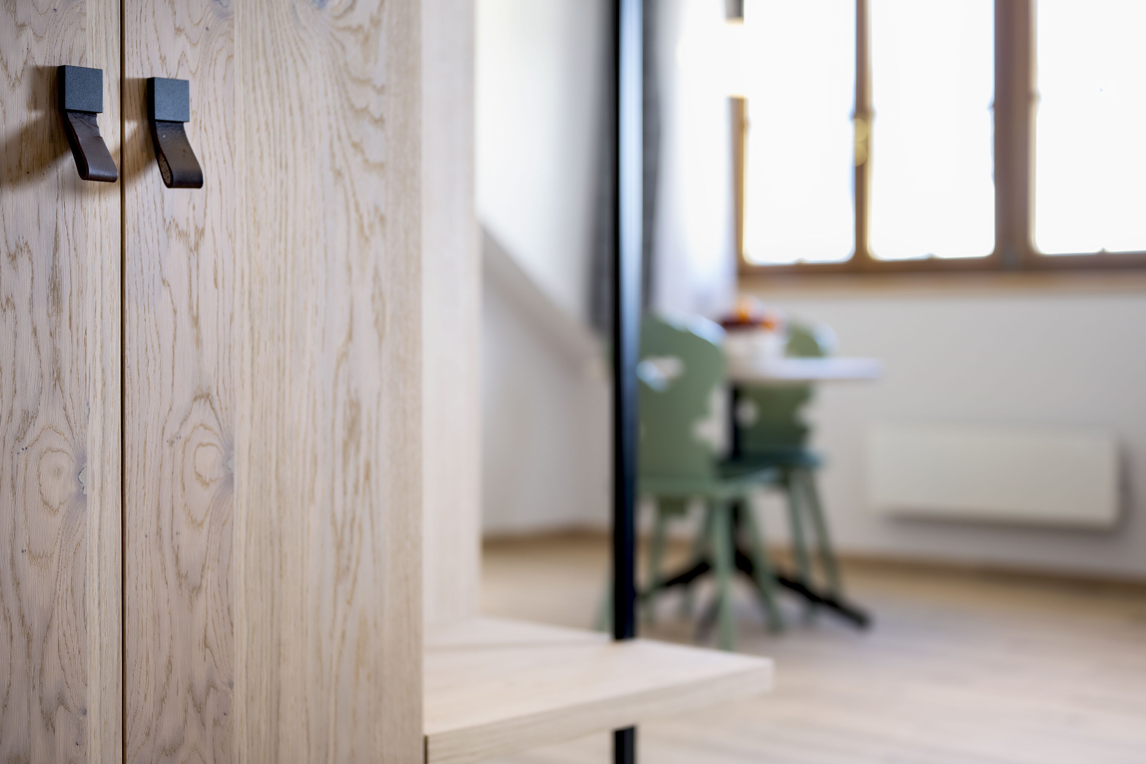 A wooden wall with a door handle and a view of a room with a table and chairs.