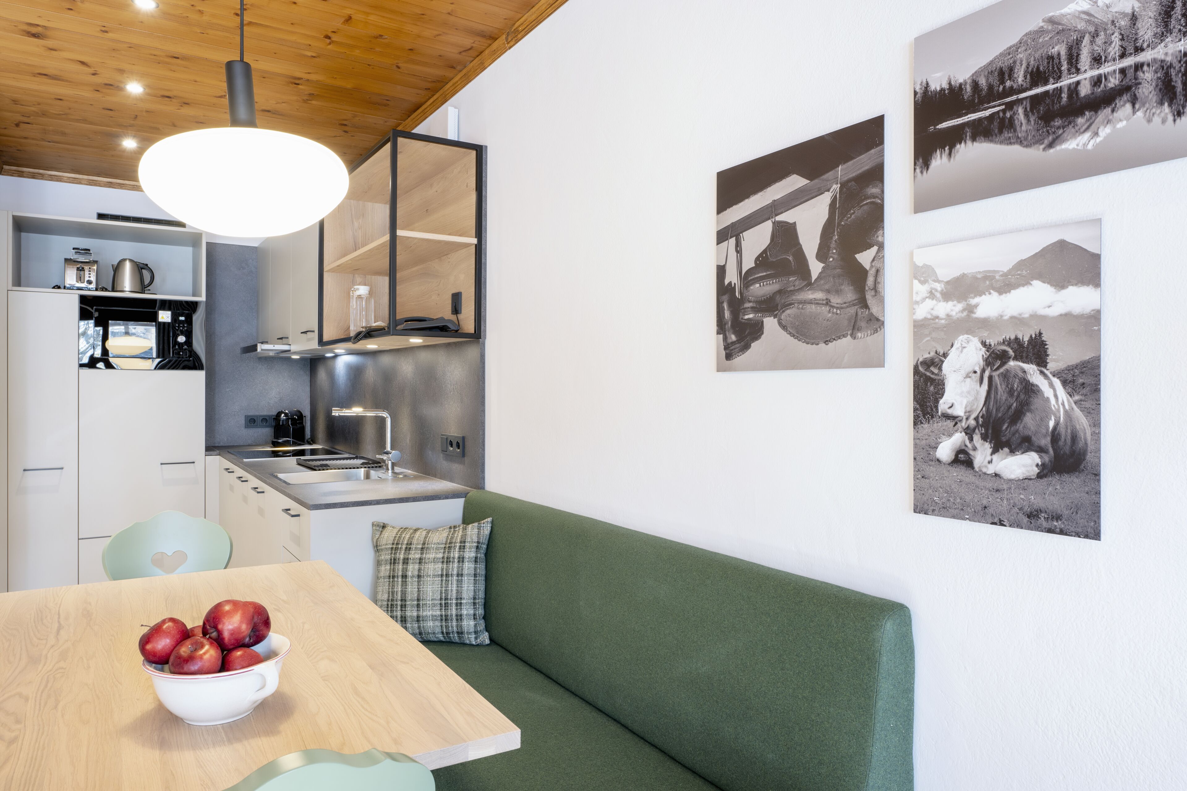A modern kitchen with a wooden ceiling, a dining table with a bowl of apples, and a green sofa.