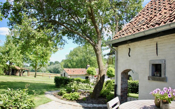 A rustic building with a tiled roof, surrounded by lush greenery and a well-maintained garden. - B&B Het Stille Genoegen (Brakel)