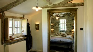 Un dormitorio con pared de piedra, una cama con colcha a cuadros, una mesita de noche, un espejo y una ventana con vistas al exterior.