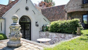 Un patio con un banco de piedra, una urna decorativa y un edificio con techo de tejas.