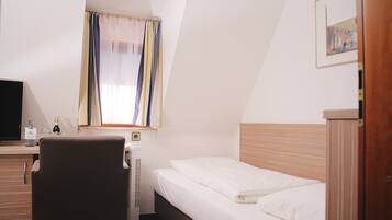 Una habitación de hotel con una cama, un escritorio con computadora, una silla, una ventana con cortinas e imagen enmarcada en la pared.