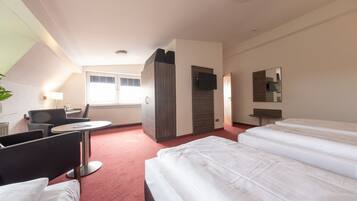 A hotel room with two beds, a desk, a chair, a TV, and a window.