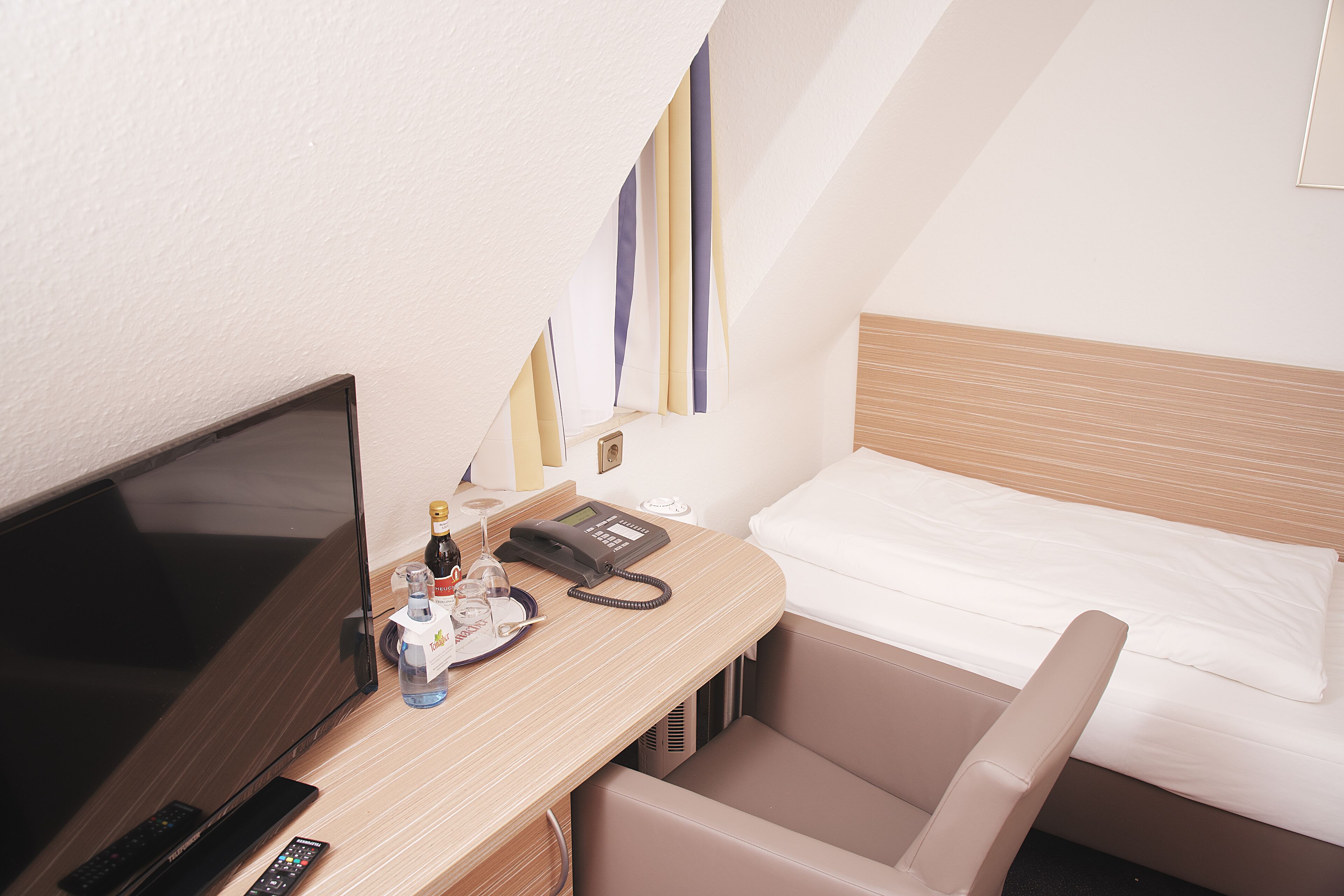 Habitación de hotel con cama, escritorio, televisor, teléfono y una botella de agua.