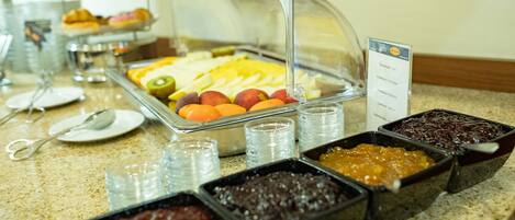 Un bufé con diversos alimentos, incluyendo frutas, pasteles y salsas.