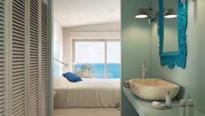 Une chambre avec une grande fenêtre, un lit, une salle de bain avec un lavabo et un miroir, et une vue sur la mer.