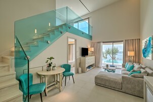 Uma sala de estar espaçosa com escada de vidro, um conjunto de sofás, uma mesa de jantar e uma televisão.