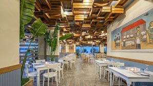 Un restaurant avec des panneaux de bois au plafond, des tables et des chaises blanches.