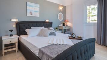 Un dormitorio ordenado con una cama grande, mesitas de noche, una lámpara de noche, un reloj de pared y una ventana con cortinas.