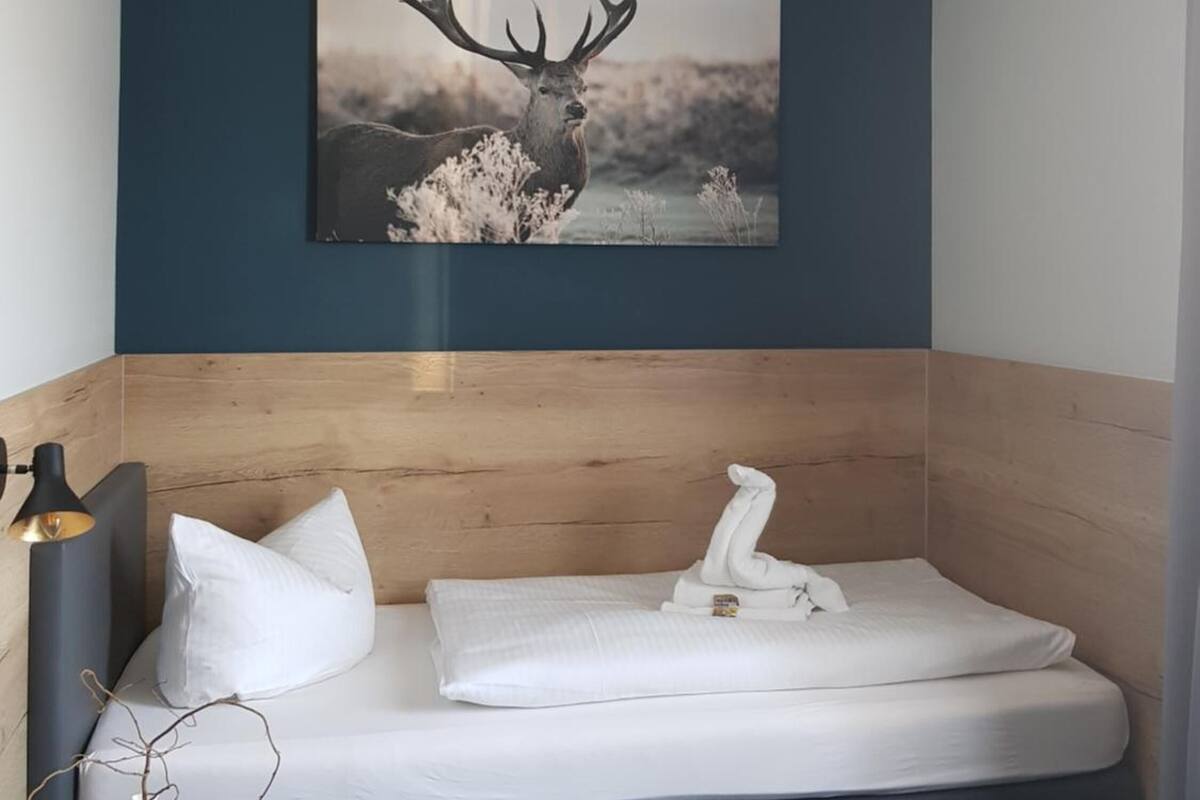 Een moderne kamer met een bed, een nachtkastje met een lamp, en een ingelijst natuurfoto aan de muur.