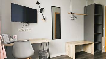 A modern office space with a desk, chair, TV, and shelving unit.