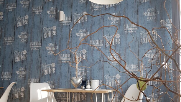 Un comedor con pared azul estampada, sillas blancas, una mesa de madera y una lámpara colgante blanca.