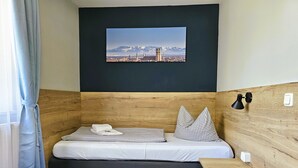 Un dormitorio con una cama, una mesita pequeña, una lámpara de pared y una fotografía de un paisaje urbano.