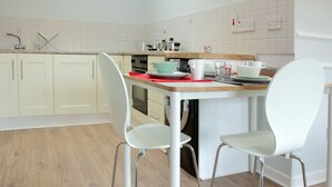 Een moderne keuken met witte kasten, een houten aanrecht en twee witte stoelen.